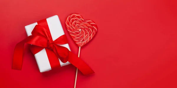 バレンタインデーグリーティングカードテンプレート 赤い背景にギフトボックスとハートキャンディーロリポップ コピースペース付きのトップビューフラットレイ — ストック写真