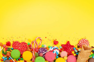 Çeşitli tatlı çeşitleri var. Şeker, bonbon ve sarı arka planda badem kurabiyesi. Üst görünüm düzlüğü kopyalama alanı ile yatıyordu