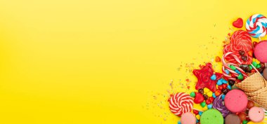 Çeşitli tatlı çeşitleri var. Şeker, bonbon ve sarı arka planda badem kurabiyesi. Üst görünüm düzlüğü kopyalama alanı ile yatıyordu