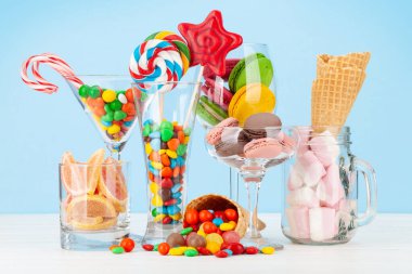 Çeşitli tatlı çeşitleri var. Şeker, bonbon, çikolata ve mavi arka planda kokteyl bardaklarında kurabiyeler.