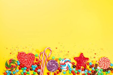 Çeşitli tatlı çeşitleri var. Sarı arka planda şeker, bonbon ve lolipop. Üst görünüm düzlüğü kopyalama alanı ile yatıyordu