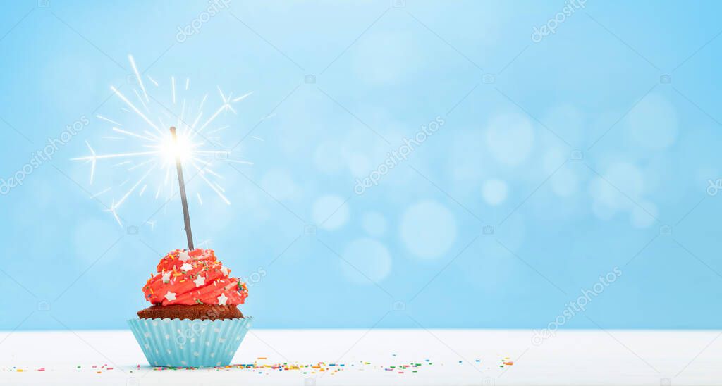 Birthday cupcake with burning sparkler over blue background with copy space for your greetings