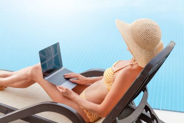 Uzaktan kontrol için dizüstü bilgisayar kullanan ya da havuz kenarında eğitim alan genç bir kadın. Metnin ya da uygulaman için kopyalama alanı ile