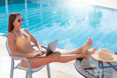 Uzaktan kontrol için dizüstü bilgisayar kullanan ya da havuz kenarında eğitim alan genç bir kadın. Metnin ya da uygulaman için kopyalama alanı ile