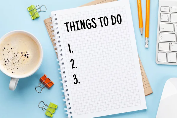 Business desk workplace with to do list notepad and office objects over blue backdrop. Top view flat lay