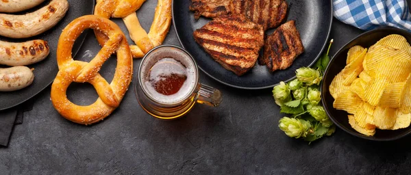 Oktoberfest seti. Krakerler, sosisler, et ve bira bardağı taştan arka planda. Üst görünüm düzlüğü