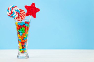 Çeşitli tatlı çeşitleri var. Şeker, bonbon, çikolata ve mavi arka planda kokteyl bardağında kurabiye. Kopyalama alanı ile