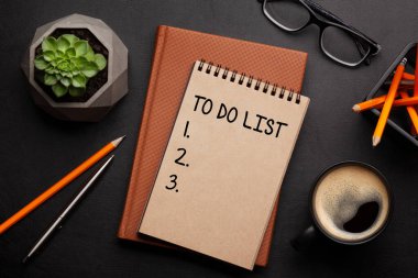 Ofis masasında malzeme ve kahve fincanı, siyah deri masanın üzerinde. Üst görünüm düz dizüstü bilgisayarı ile yapılacaklar listesi ile yatıyordu