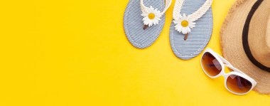 Yaz tatili eşyaları ve aksesuarları. Parmak arası terlik, güneş gözlüğü ve sarı arka planda güneş şapkası. Üst görünüm düzlüğü kopyalama alanı ile yatıyordu