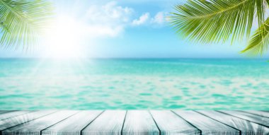Dalgalar, palmiye yaprakları ve bulutlu mavi gökyüzü ile tropikal yaz denizi. Boş ahşap masa ile mükemmel bir tatil manzarası.