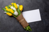 Barevné tulipánové květiny a prázdné přání na kamenném pozadí. S kopírkou. Horní pohled rovný