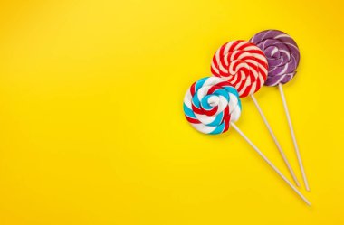 Çeşitli tatlı çeşitleri var. Sarı arka planda şeker ve lolipoplar. Üst görünüm düzlüğü kopyalama alanı ile yatıyordu