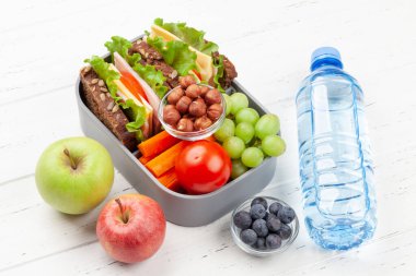 Sandviç, taze sebze, su şişesi, fındık ve meyveli sağlıklı okul beslenme çantası.
