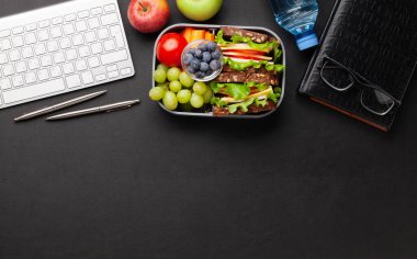 Sandviçli, taze sebzeli, su şişeli, fındıklı ve meyveli sağlıklı bir yemek kutusu. Üst görünüm düzlüğü kopyalama alanı ile yatıyordu