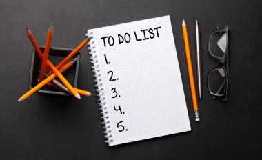 Liste defteri, malzeme ve gözlüklerle dolu bir ofis masası. Üst görünüm düzlüğü kopyalama alanı ile yatıyordu