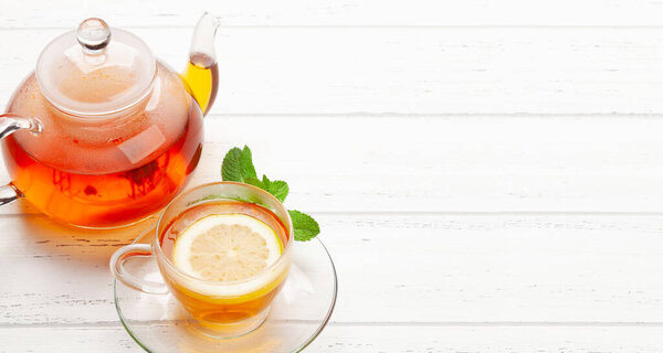 Травяной чай с мятой и лимоном. Чашка чая и чайник на деревянном столе. С копировальным местом