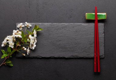 Kiraz çiçekleri ve suşi çubukları olan Japon yemekleri. Üst görünüm besin veya metin için taş tahta ile düz yatıyordu