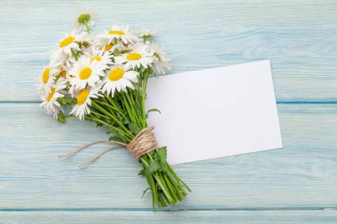 Bahçede papatya çiçeği buketi ve mavi ahşap masada tebrik kartı. Üst görünüm düzlüğü kopyalama alanı ile yatıyordu