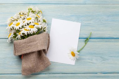 Ahşap masada papatya çiçeği buketi ve tebrik kartı şablonu. Üst görünüm düzlüğü kopyalama alanı ile yatıyordu