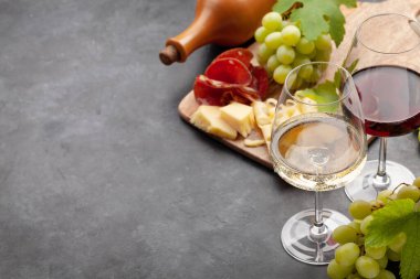 Beyaz ve kırmızı şarap bardakları, eski taş masada peynir ve jambonlu üzüm ve aperatif. Kopyalama alanı ile