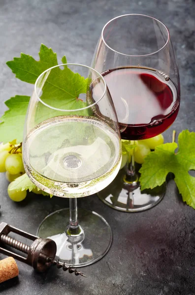 Beyaz ve kırmızı şarap kadehleri, üzüm ve eski taş masanın üzerinde eski bir tirbuşon.