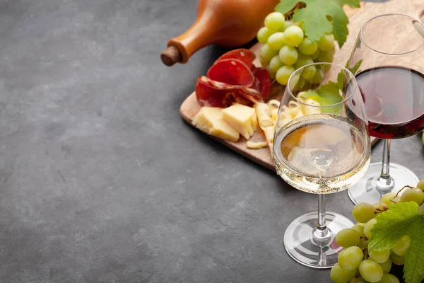 Beyaz ve kırmızı şarap bardakları, eski taş masada peynir ve jambonlu üzüm ve aperatif. Kopyalama alanı ile