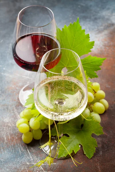 Eski taş masada beyaz ve kırmızı şarap kadehleri ve üzüm.