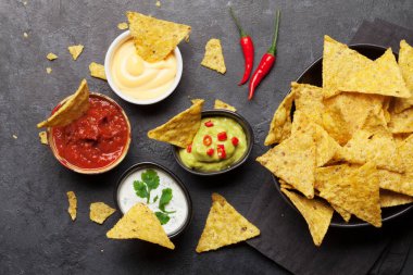 Çeşitli soslu Meksika cipsi. Guacamole, salsa, peynir ve ekşi krema. Üst görünüm düz taş masa üzerinde yatıyordu