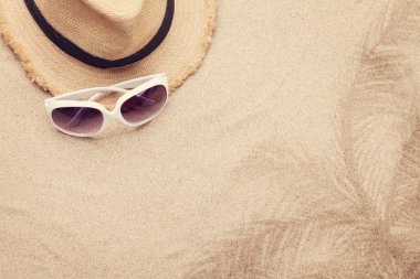 Güneş gözlüklü, kumlu arka planda şapka takan seyahat konsepti. Kopyalama alanı olan üst görünüm. Düz yatıyordu