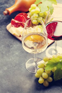 Beyaz ve kırmızı şarap bardakları, üzüm ve aperatif panosu peynir ve jambonlu.