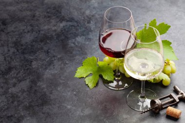 Beyaz ve kırmızı şarap kadehleri, üzümler ve eski taş masanın üzerindeki tirbuşon ve fotokopi alanı.