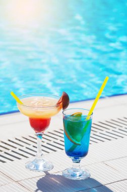 Yüzme havuzunun kenarında iki renkli kokteyl bardağı. Kopyalama alanı ile
