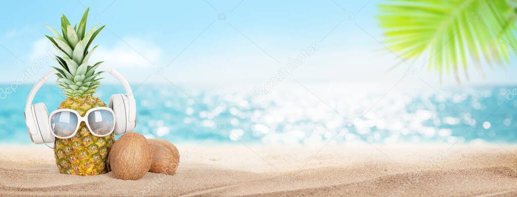 Summer tropical sea with sparkling waves, pineapple with sunglasses and headphones on hot sand beach. Travel and vacation concept with copy space