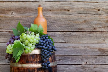 Çeşitli renkli üzümler ve şarap fıçısında şarap şişesi açık havada güneşli bahçede ahşap duvarın önünde fotokopi alanı olan