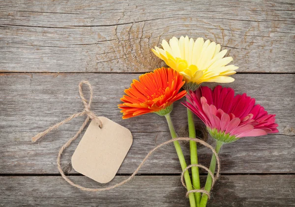 Three colorful gerbera flowers with tag — Stock Photo, Image