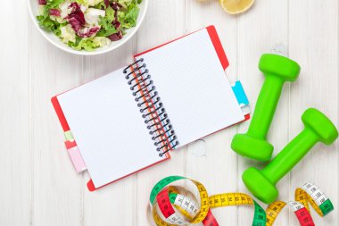 Dumbells, mezura, sağlıklı yiyecek ve not defteri
