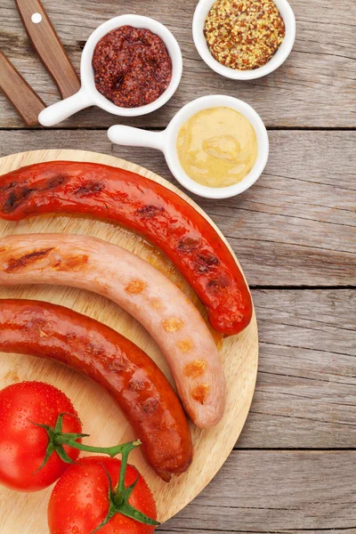 Various grilled sausages with condiments and tomatoes — Stock Photo, Image