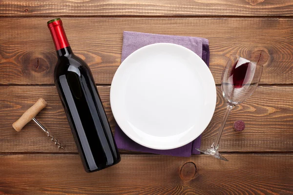 Plate, wine glass and red wine bottle — Stock Photo, Image