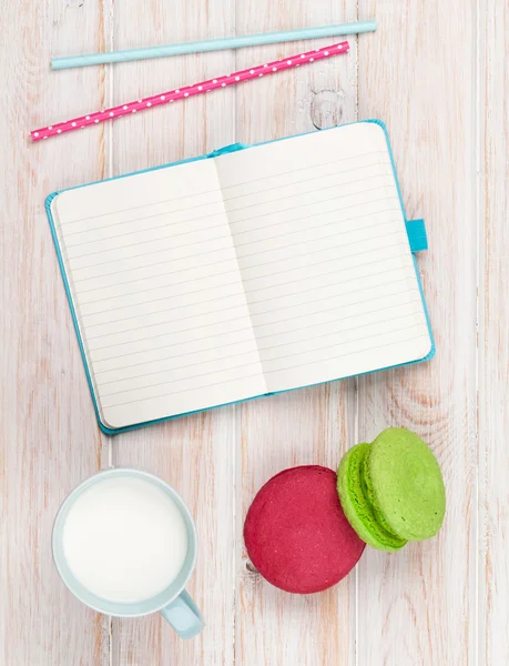 Tasse Milch und Macarons auf weißem Holztisch mit Notizblock — Stockfoto