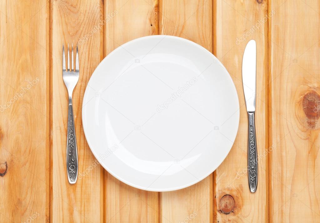 Empty plate and silverware over wooden table background