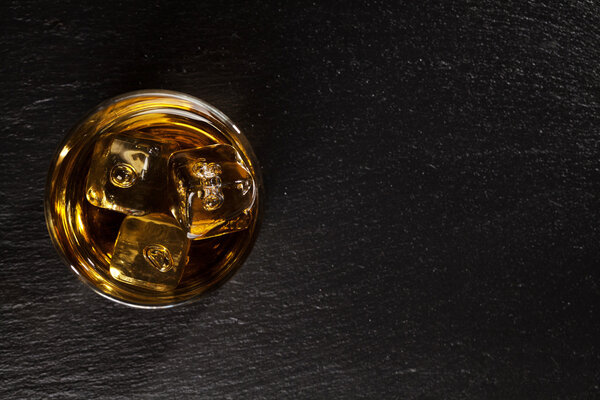 Glass of whiskey with ice on black stone