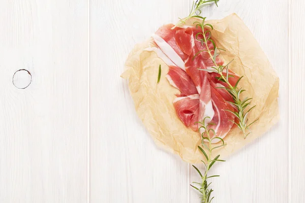 Prosciutto with rosemary on wooden table — Stock Photo, Image