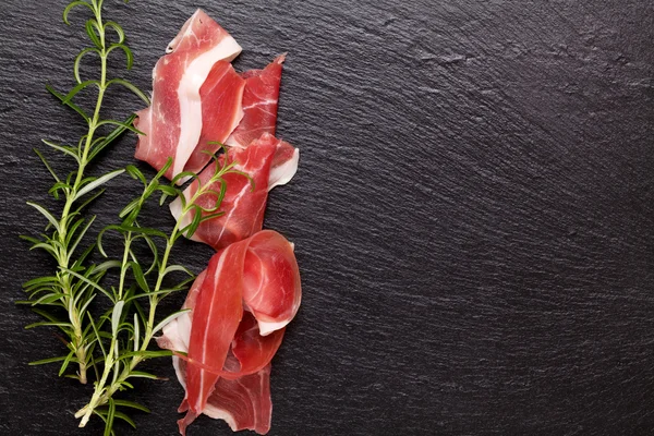 Prosciutto with rosemary on stone table — Stock Photo, Image