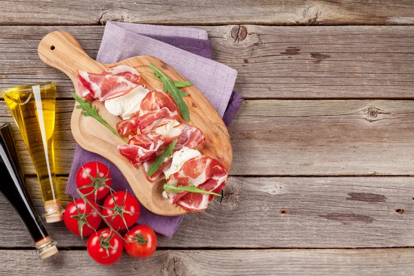 Prosciutto, mozzarella and tomatoes and bottles of oil — Stock Photo, Image