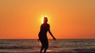 Gün batımında kumsalda zıplayan mutlu kadın.