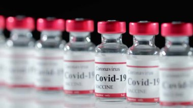 Doktorlar lateks eldivenleri teslim ederken masadan Covid-19 aşı şişesi alıyor.