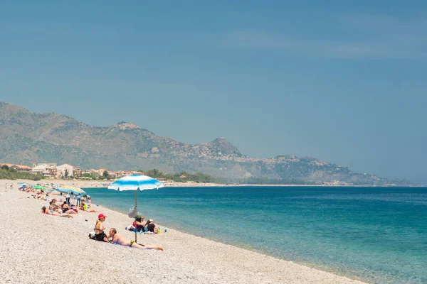 Personnes non identifiées sur la plage à Giardini Naxos avec Taormina ville en arrière-plan, Sicile — Photo