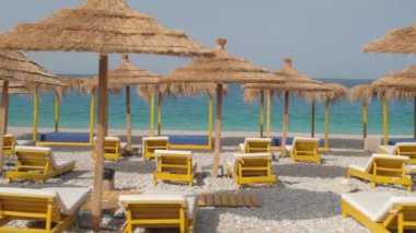 Kamera, şemsiyeler ve güneşliklerle güzel sahilde yavaşça hareket ediyor.