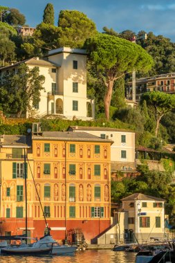İtalya 'nın Liguria kentindeki Portofino tatil beldesinin günbatımı manzarası. Ligurian kıyıları boyunca tarihi renkli binalarla çevrili demirlemiş yelkenlileri ve lüks yatları olan büyüleyici bir liman..
