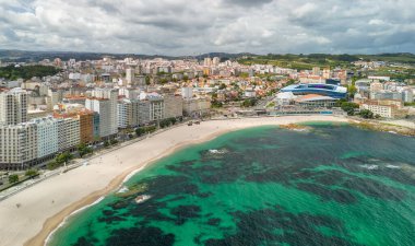 A Coruna, Galiçya, İspanya 'da güneşli bir günde Playa del Orzan plajının hava manzarası. Şehir merkezinde canlı turkuaz deniz suyuyla dolu uzun kumlu bir sahil. Kuzey İspanya 'da halk seyahati